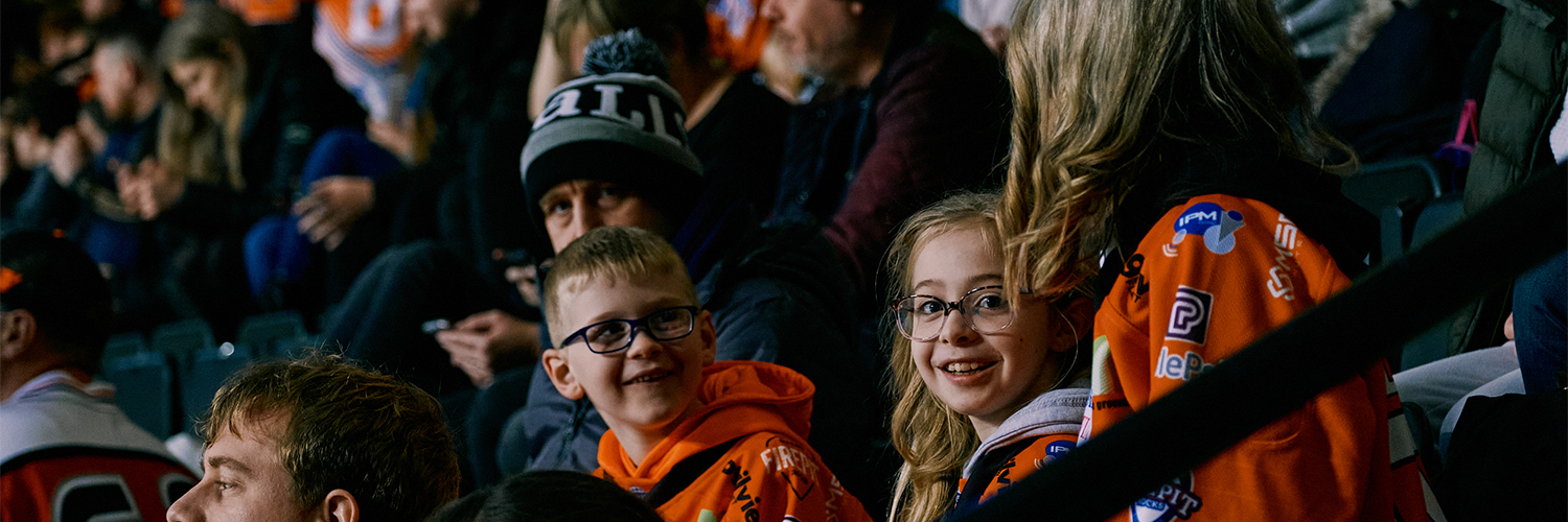 A section of people including 2 children smiling at the ice hockey game sheffield